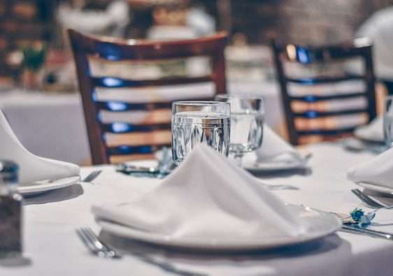 depth of field photo of clear drinking glass on white table near plate